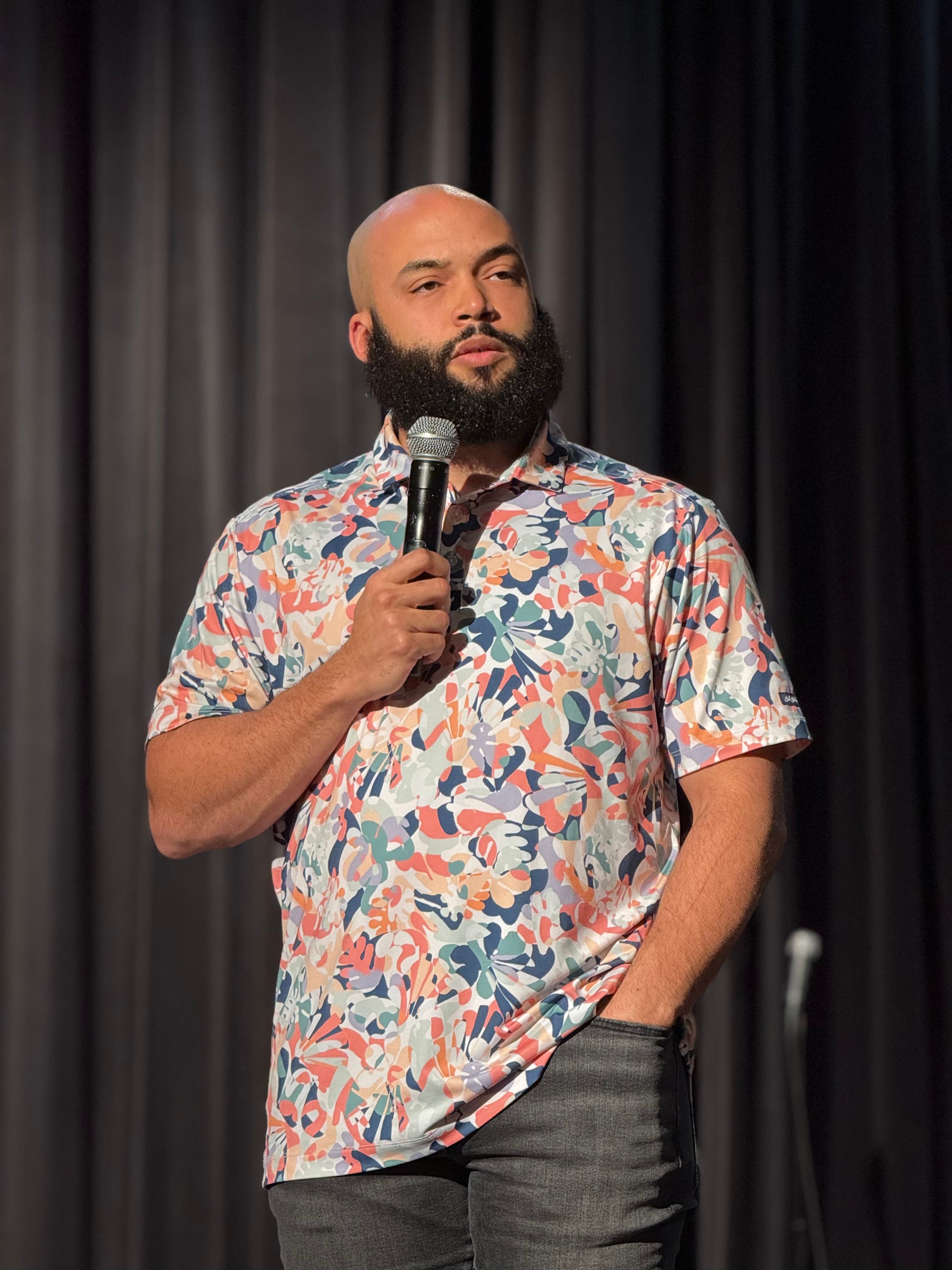 Blake M. Jones with a handheld microphone against a dark stage curtain